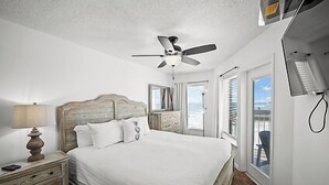 Un dormitorio con cama, mesitas de noche, ventilador de techo y ventana con persianas.