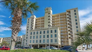 Un hotel de varios pisos con balcones, una torre central y un estacionamiento con coches.