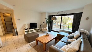 Ein modernes Wohnzimmer mit Sofa, Couchtisch, Fernseher und einem großen Fenster mit Blick.