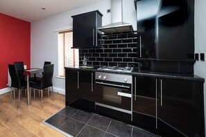 Een moderne keuken met zwarte kastjes, een roestvrijstalen oven en een eethoek met een rode muur en zwarte stoelen.