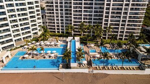 Un resort con varias piscinas, palmeras y edificios altos al fondo.