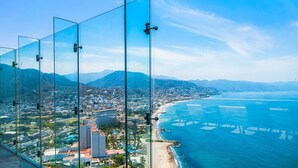 Un paisaje costero con playa, montañas y una vista a través de un panel de vidrio.