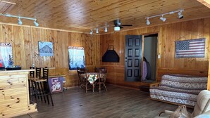A cabin interior with a dining area, a sofa, and a wooden floor. - Spacious Mio Cabin - Sleeps 20+ - Game Room - Near AuSable River & ORV Trails (Mio)
