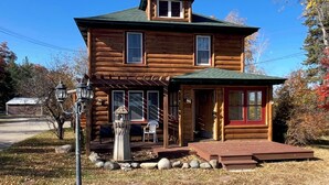 A two-story log cabin with a porch, a small attached shed, and a stone pathway leading to the entrance. - Spacious Mio Cabin - Sleeps 20+ - Game Room - Near AuSable River & ORV Trails (Mio)