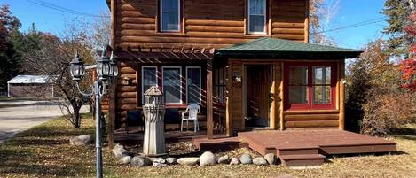 A two-story log cabin with a porch, a small attached shed, and a stone pathway leading to the entrance.