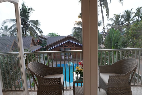 A balcony with wicker chairs, a small pool, and a view of a wooden building with a sloped roof. - Foxoso Aaristo Baga Beach Resort (Baga)