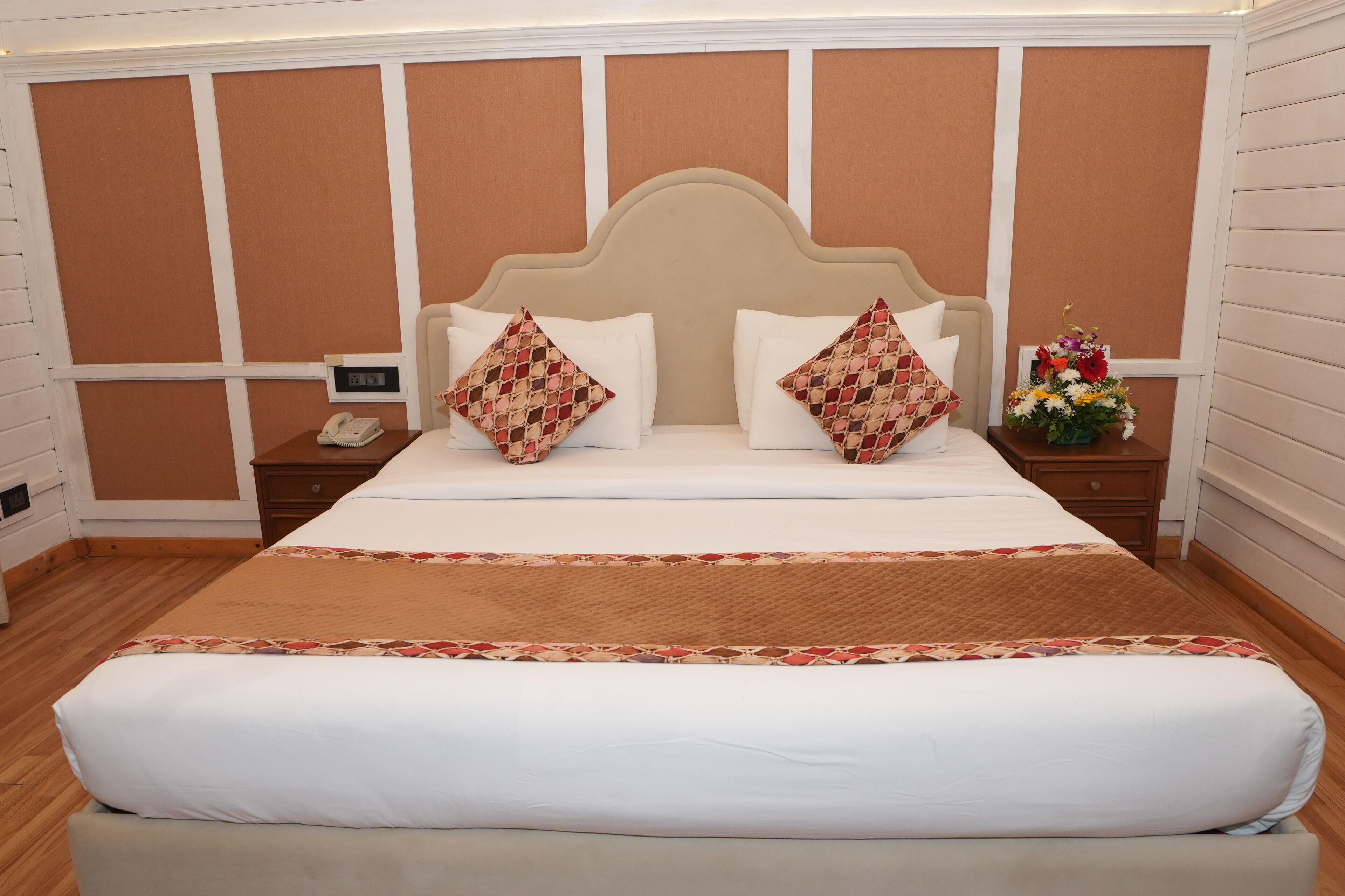 Une chambre d’hôtel avec un grand lit, deux tables de chevet, une petite table, un téléphone et un arrangement floral.