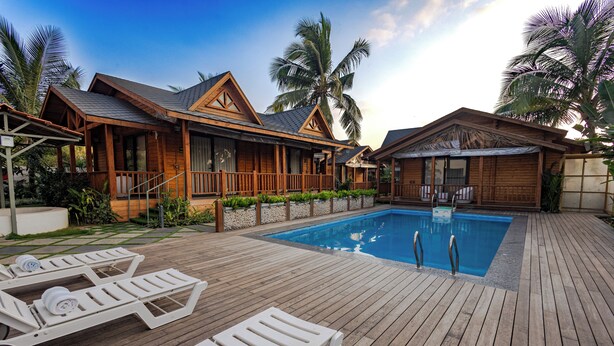 Una villa in legno con piscina, lettini prendisole e palme.