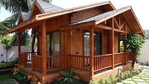Una baita di legno con veranda, circondata da piante tropicali e un sentiero in pietra.