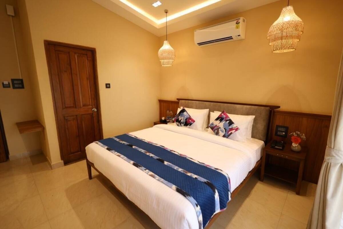 A bedroom with a large bed, wooden headboard, two bedside tables with lamps, an air conditioning unit, and a door.