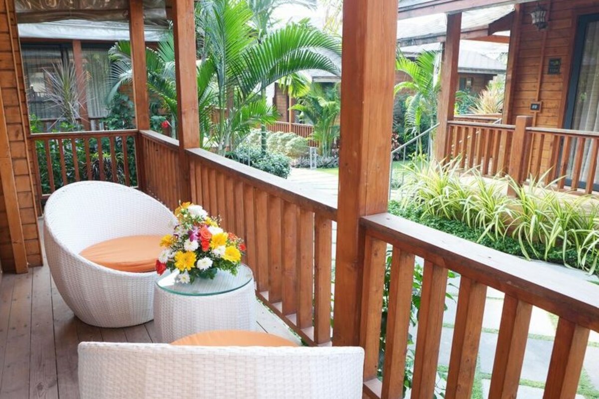 Una terraza de madera con mobiliario de mimbre y una mesa de vidrio con un centro de mesa floral.