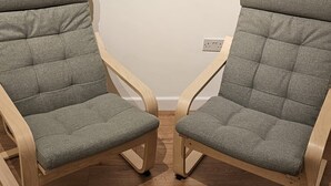 Zwei graue Polsterstühle mit Holzgestellen und geschwungenen Rückenlehnen stehen auf einem Holzboden vor einer schlichten Wand.