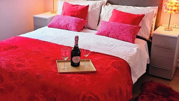 Ein Schlafzimmer mit einem Bett, einem Nachttisch, einer Lampe, einer Weinflasche und einem roten Teppich.