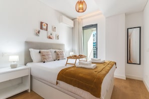 Quarto de hotel moderno com cama, mesa de cabeceira, abajur, obra de arte e vista para a cidade.