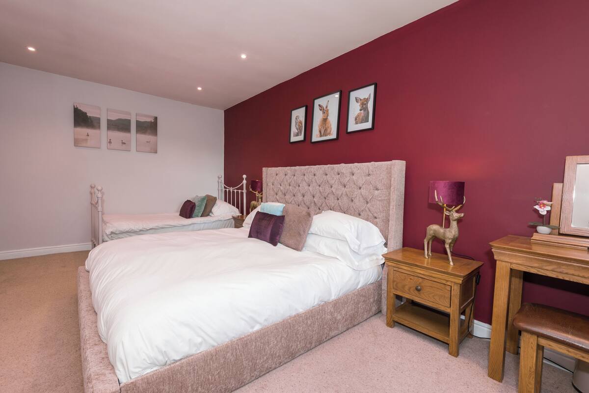 A bedroom with a large bed, a smaller bed, a nightstand, a desk, and a chair.