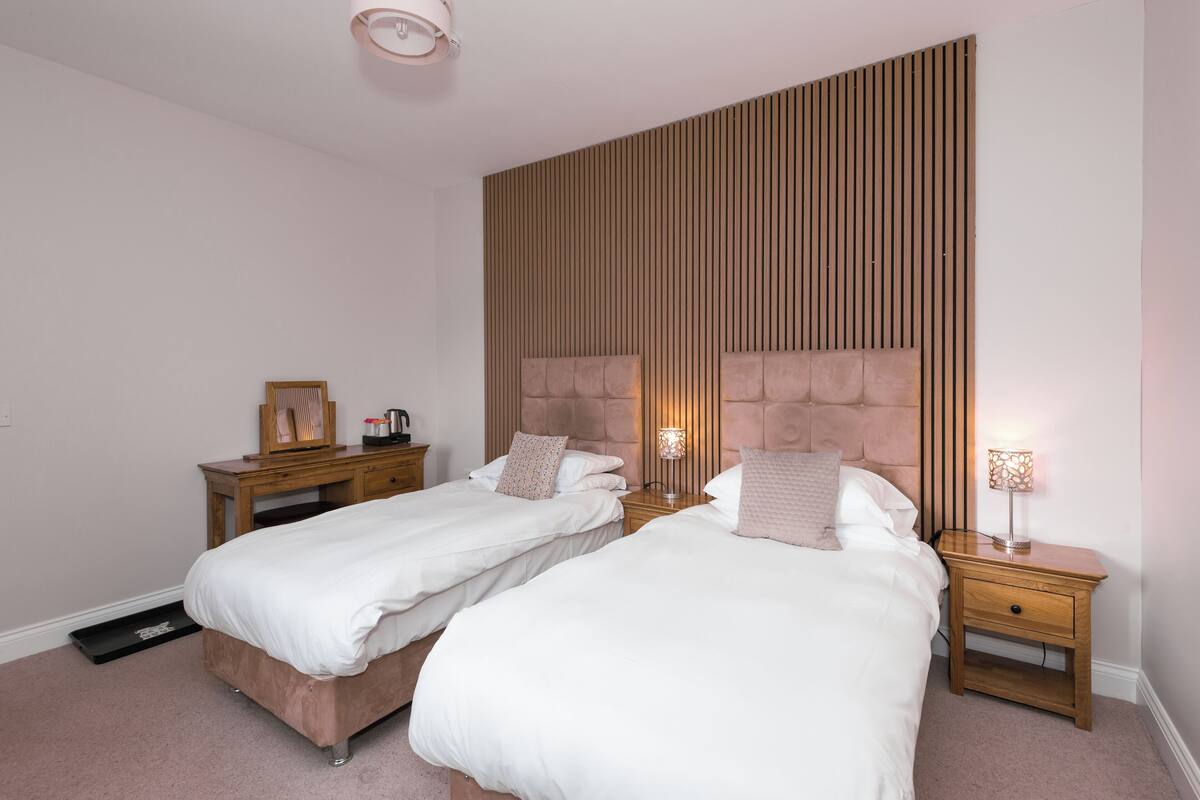 A bedroom with two single beds, wooden headboards, bedside tables, and a wall-mounted light fixture.