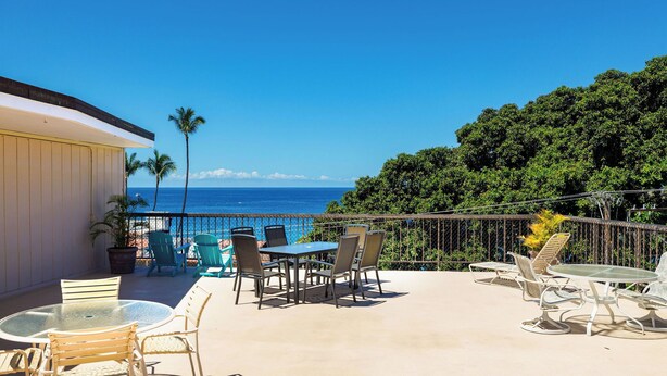 Une terrasse dotée de mobilier d’extérieur, offrant une vue sur l’océan et s’ouvrant sur un paysage verdoyant.