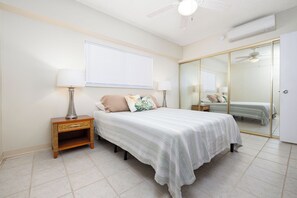 A bedroom with a bed, nightstands, a mirror, and a sliding door closet. - Kona Plaza#302: Third Floor, Ocean View in Heart of Kona Town, Ac & Elevators (Kailua Kona)