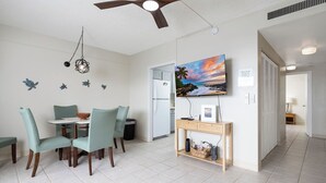 Une cuisine moderne avec un coin repas, un ventilateur de plafond, un téléviseur fixé au mur et une vue sur l’océan par la fenêtre.