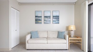 Une pièce avec un canapé à rayures, une petite table avec une lampe et trois œuvres d’art encadrées accrochées au mur.