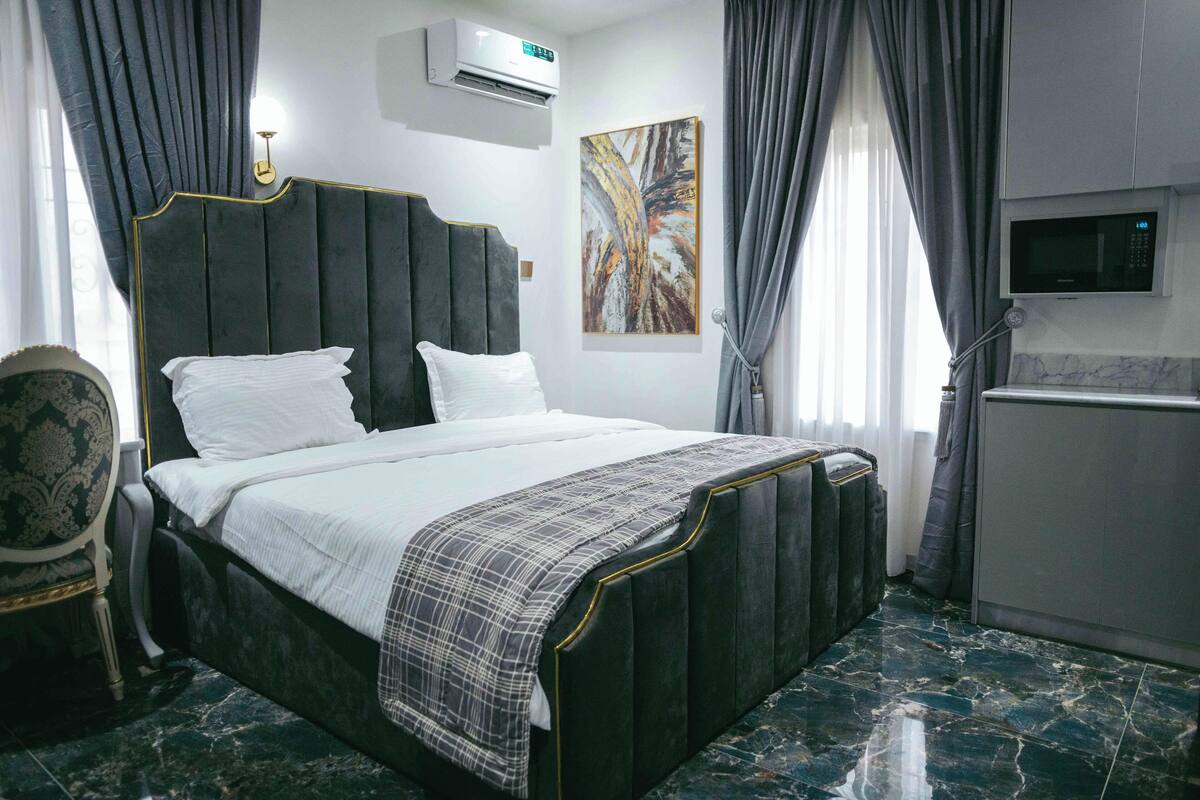 A hotel room with a large bed, a television, an air conditioning unit, and a marble floor.