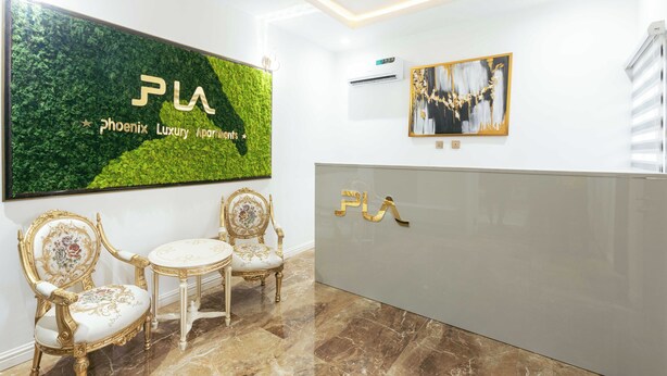 A reception area with a large 'PLA' sign, two ornate chairs, a small table, and a modern air conditioning unit. - Phoenix Luxury Apartments  (Abuja)