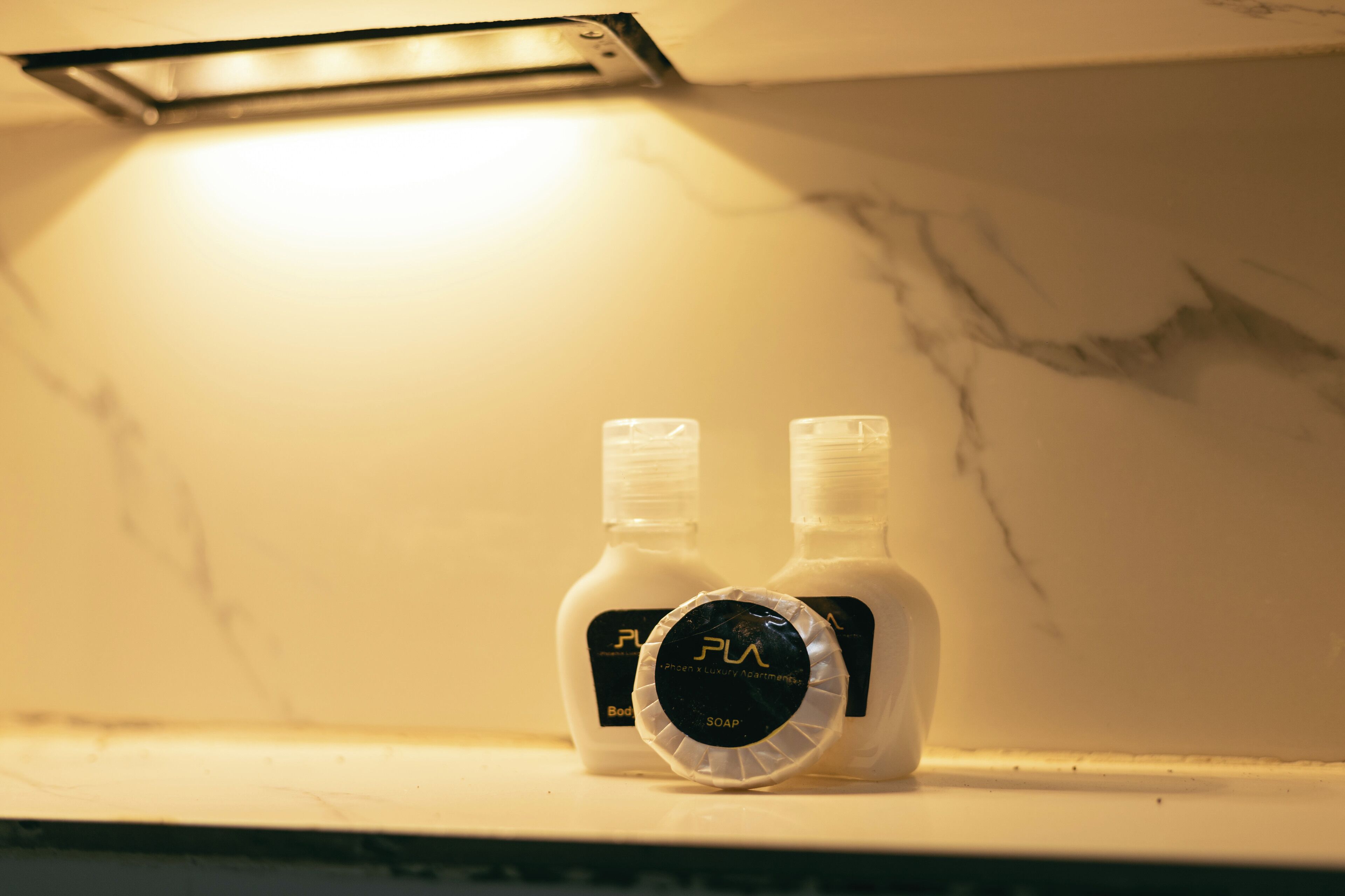 Two bottles of FLA soap on a marble countertop under a light fixture.