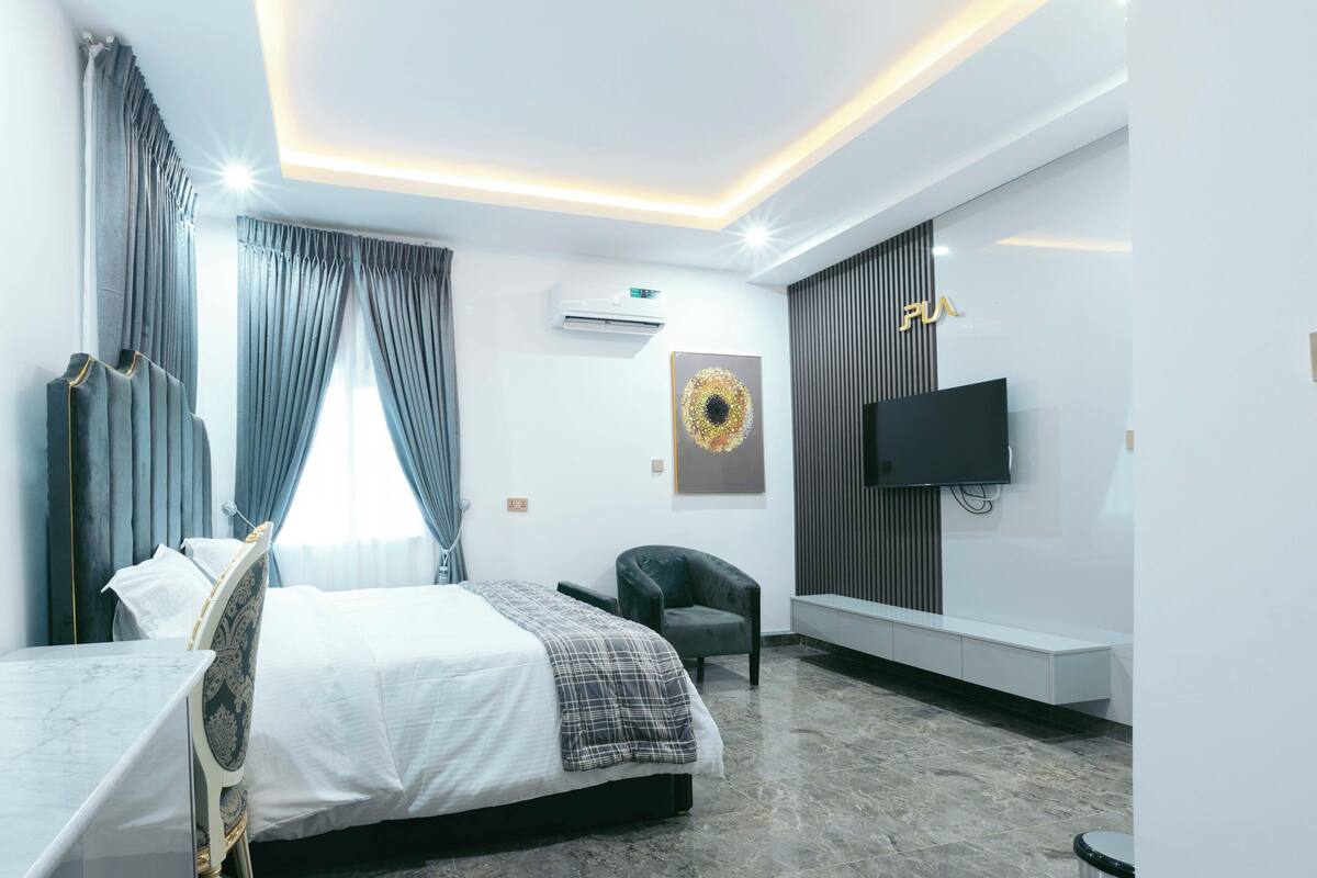 A modern hotel room with a bed, a chair, a TV, and a wall-mounted air conditioner.