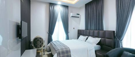 A modern hotel room with a large bed, a TV, a desk, and a chair.