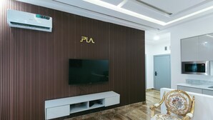 A modern living room with a flat-screen TV mounted on a wooden wall, a built-in air conditioner, and a decorative chair with intricate designs. - Phoenix Luxury Apartments  (Abuja)