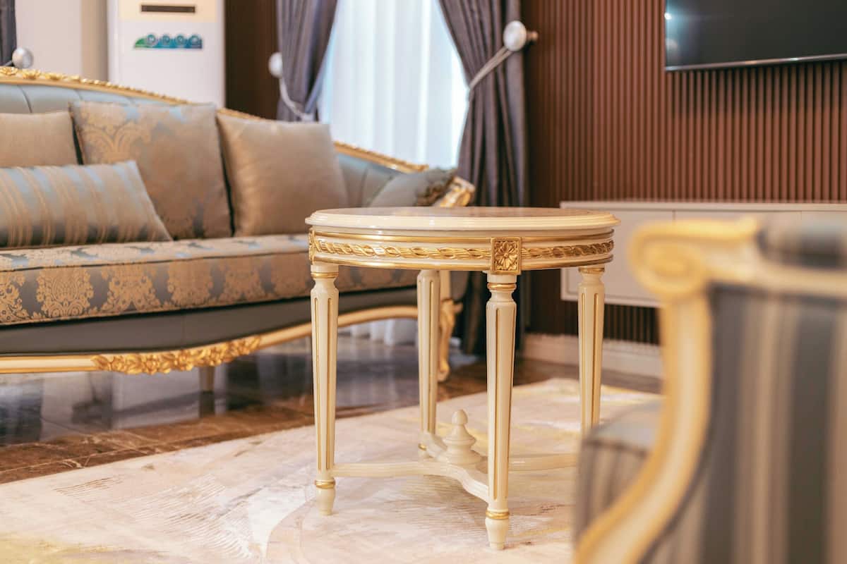 A luxurious living room with a patterned sofa, a round coffee table with ornate legs, and a television mounted on a wooden wall.