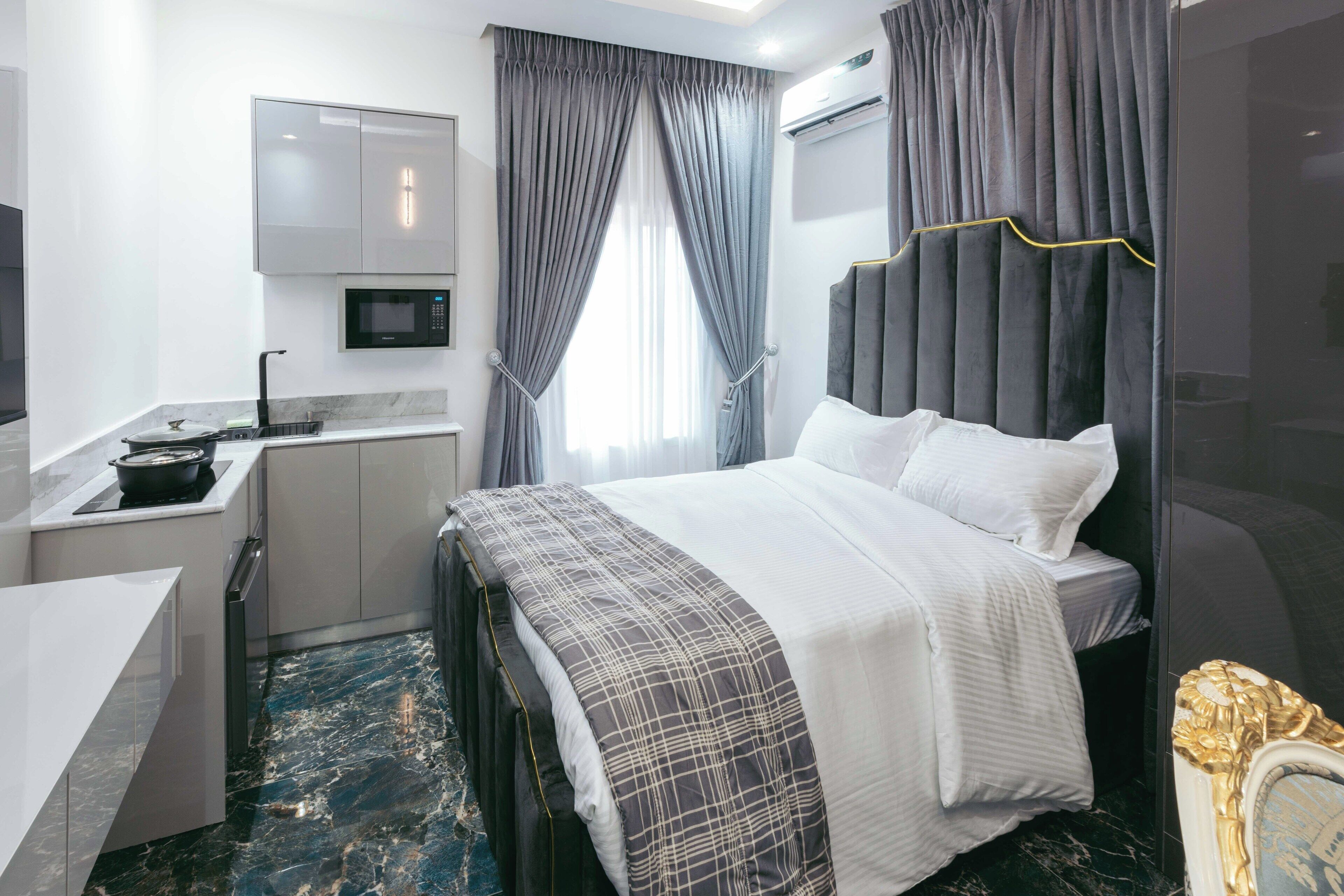 Moderni hotellihuone, jossa on sänky, yöpöytä ja pieni keittokomero.