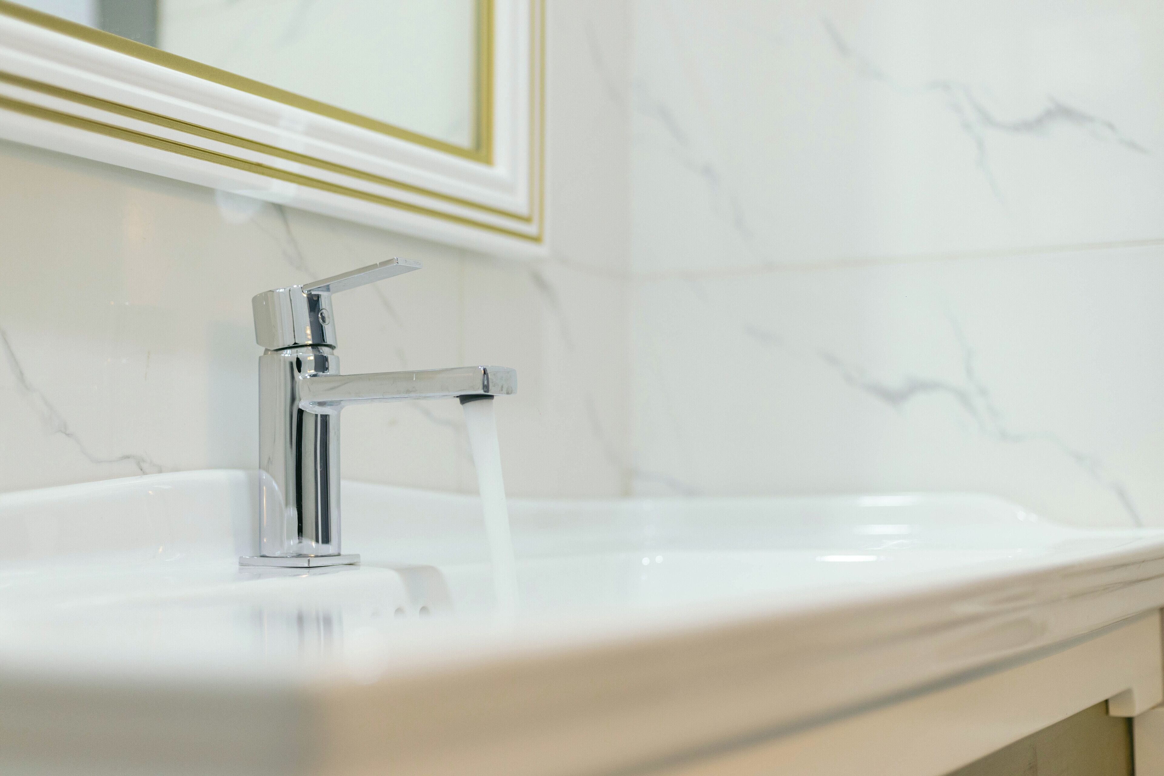 A bathroom with a white sink, chrome faucet, and marble walls.