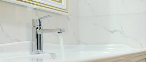 A bathroom with a white sink, chrome faucet, and marble walls.