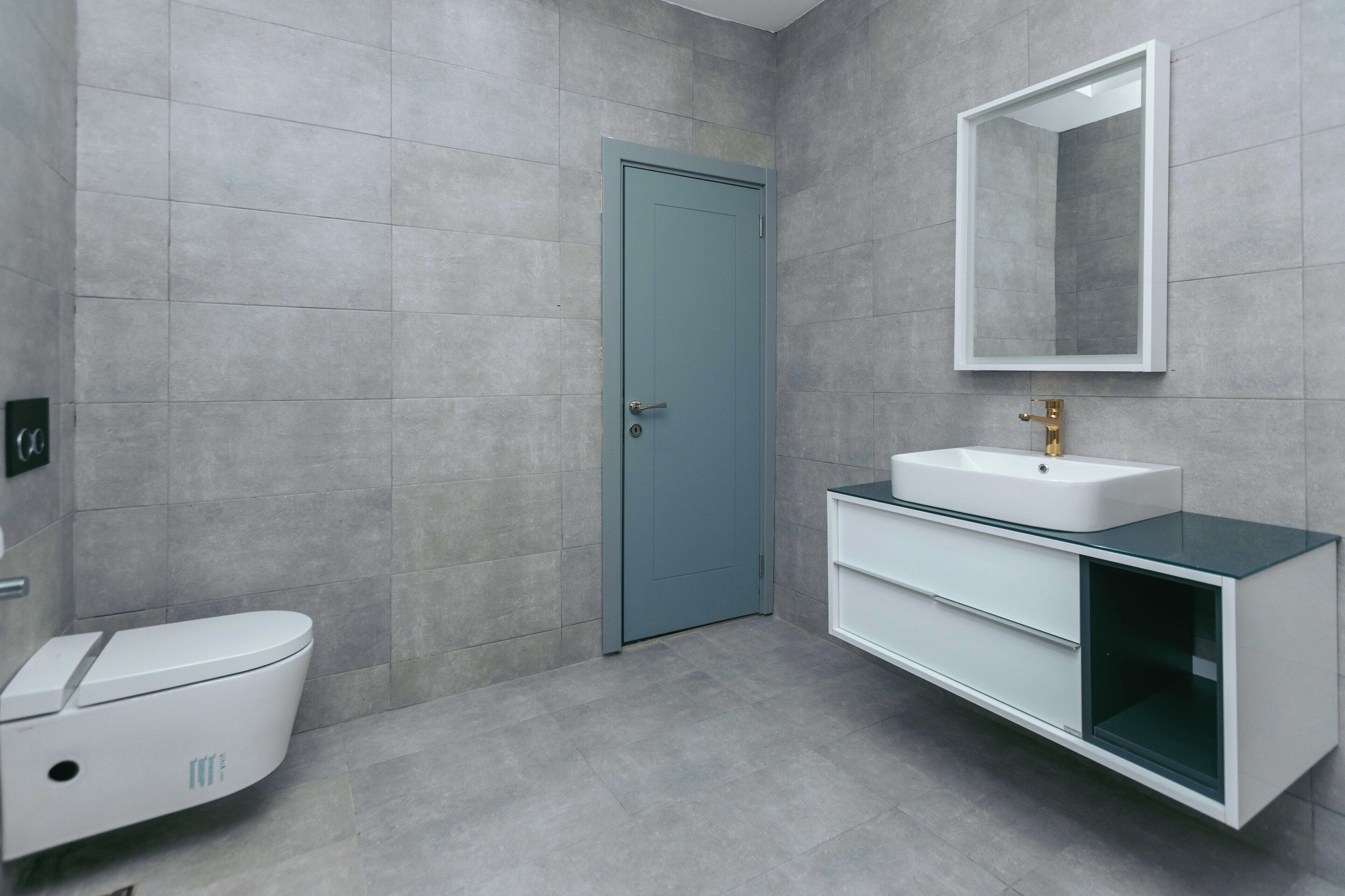A modern bathroom with a toilet, a sink with a mirror, and grey tiled walls.