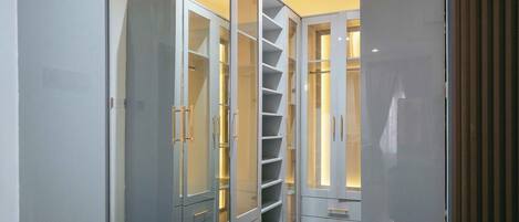 A walk-in closet with multiple shelves and drawers, featuring a modern design with metallic handles and illuminated shelves.