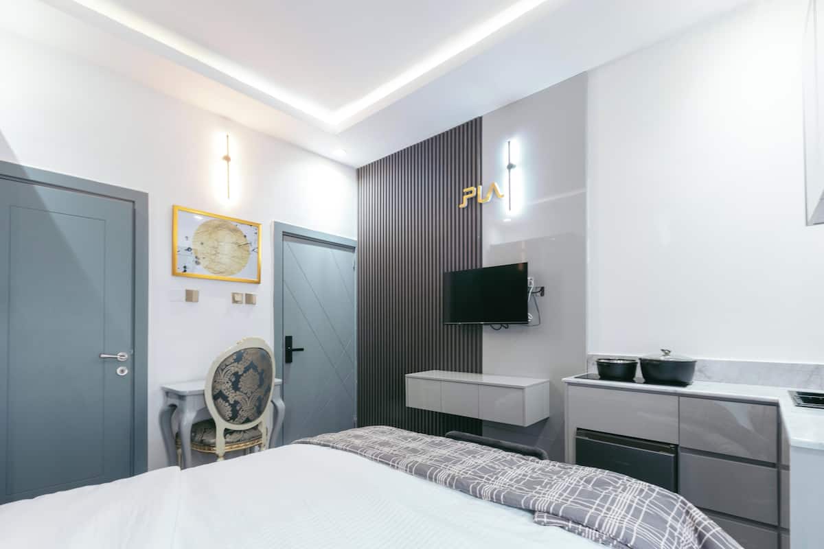 A modern hotel room with a bed, a vanity with a mirror, a television, and a small table with chairs.