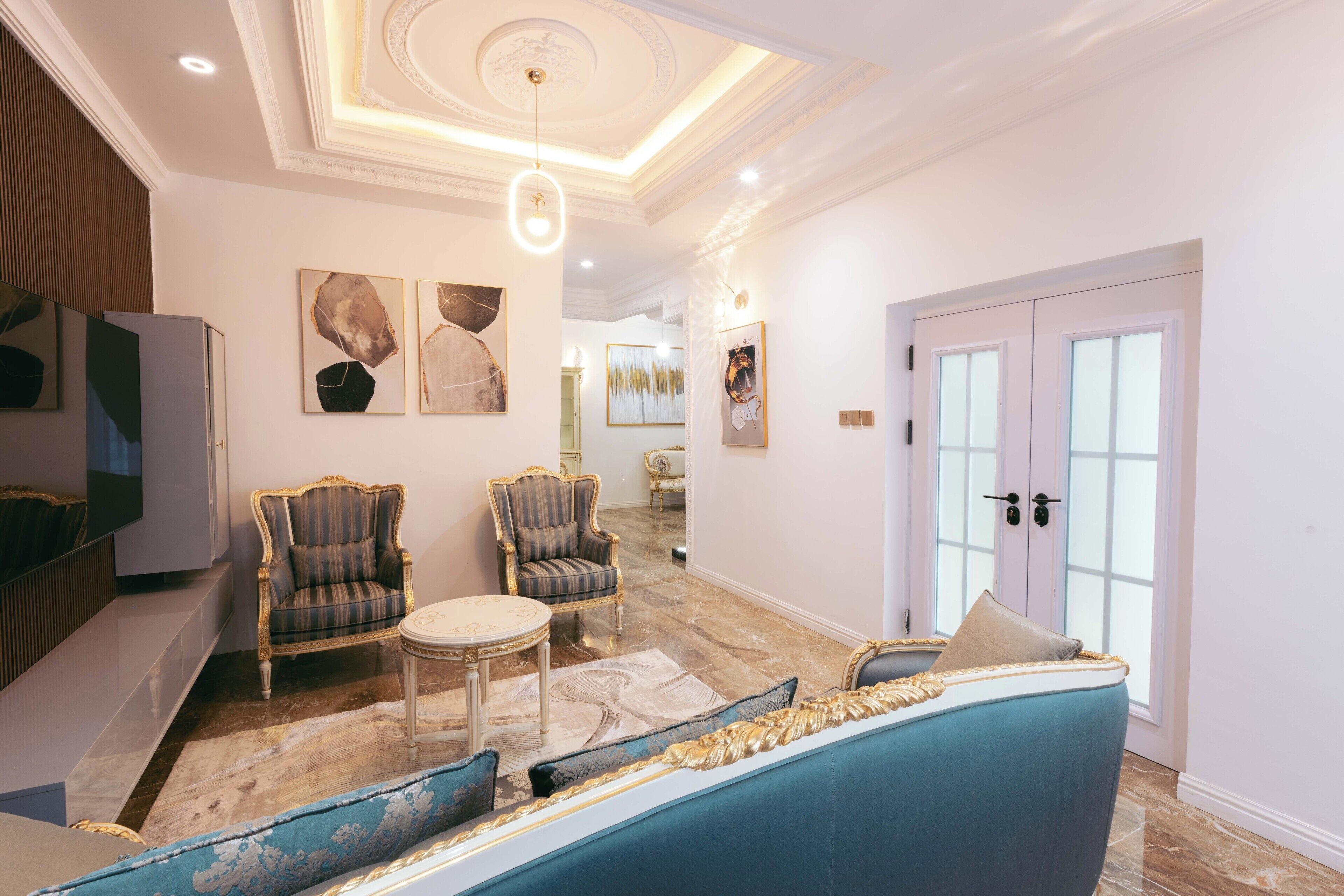 A spacious living area with a blue sofa, two armchairs, a small round table, and a decorative rug.