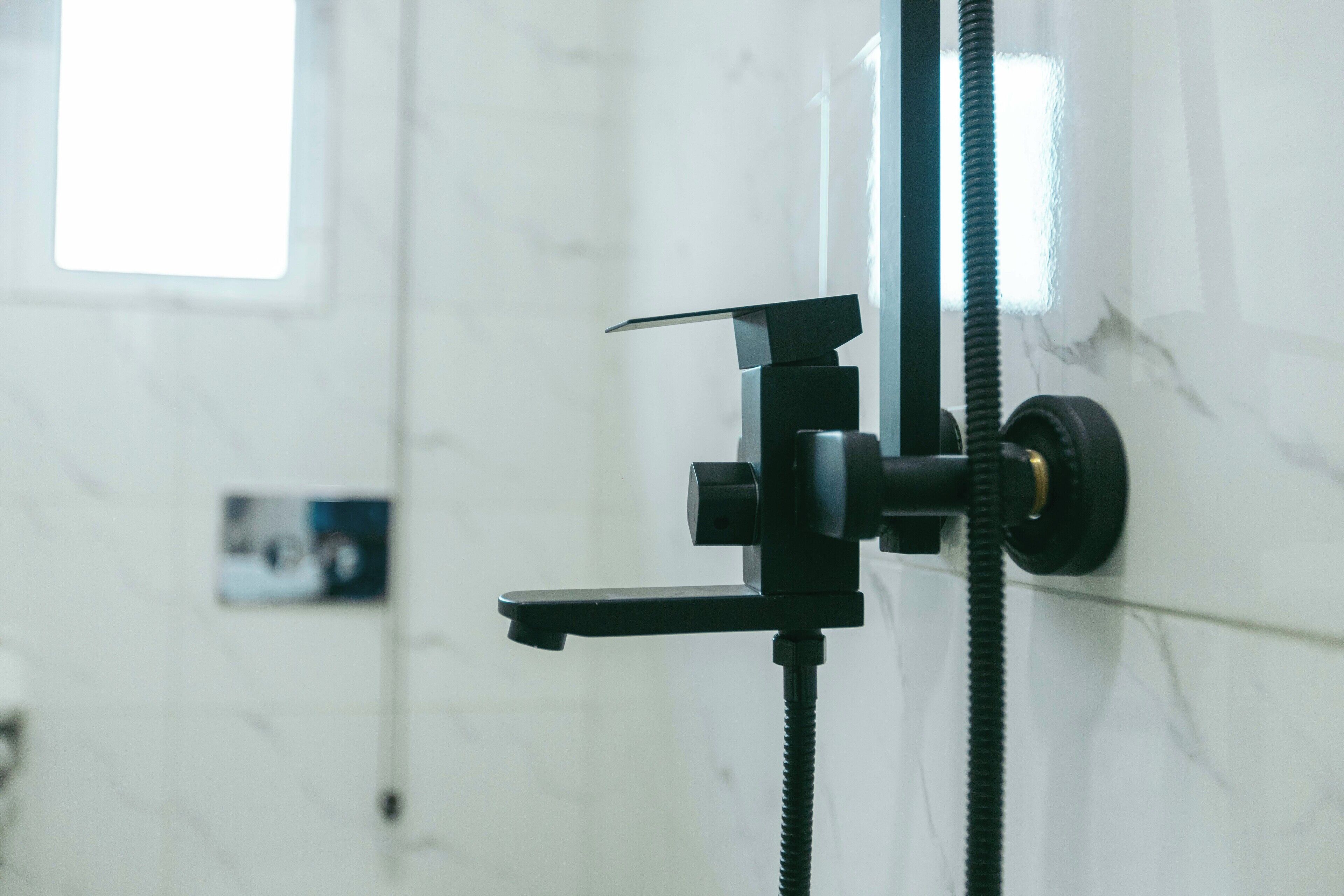 A bathroom with a shower head mounted on a wall, a towel rack, and a visible window.
