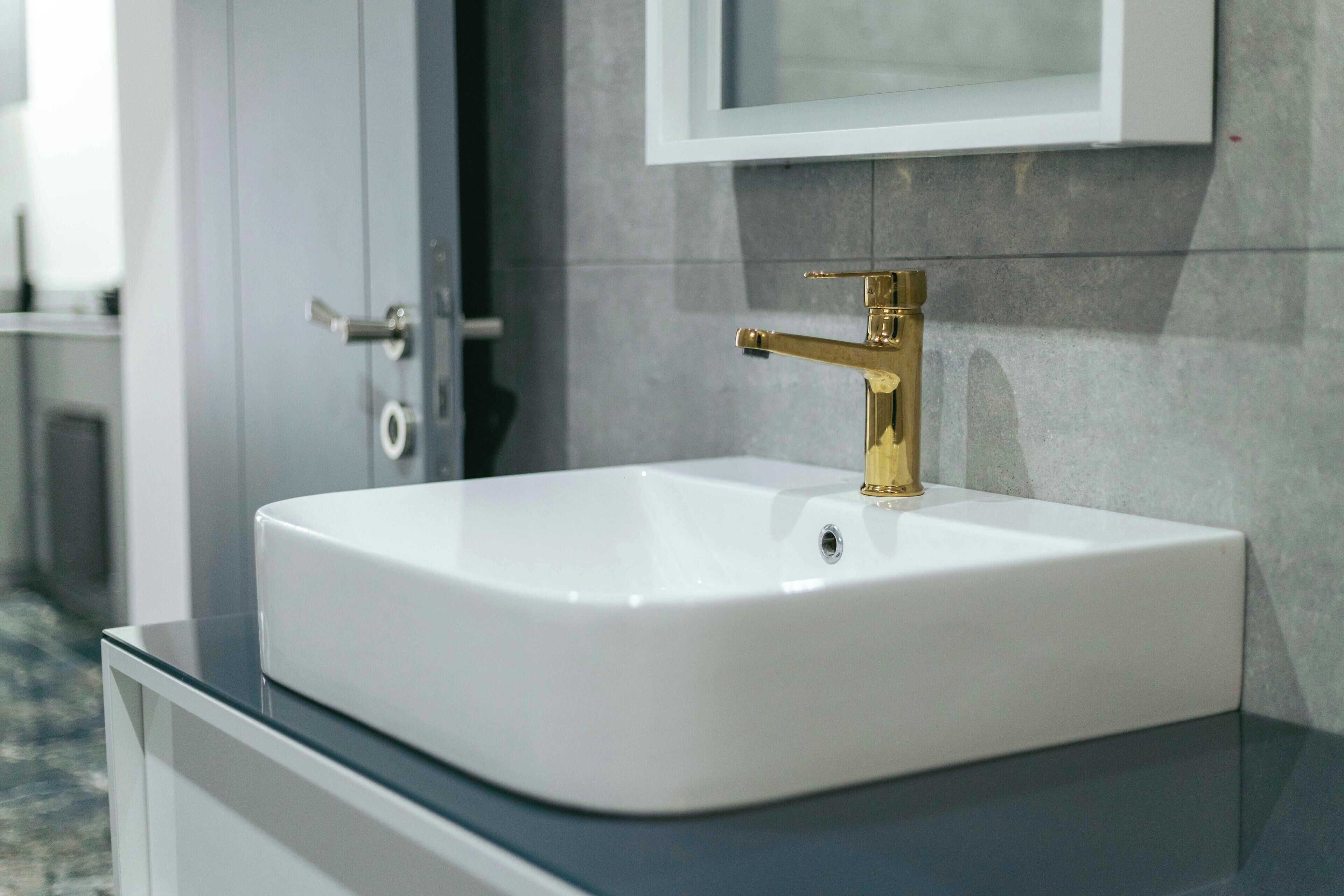 A bathroom with a white sink, gold faucet, and a mirror above it.