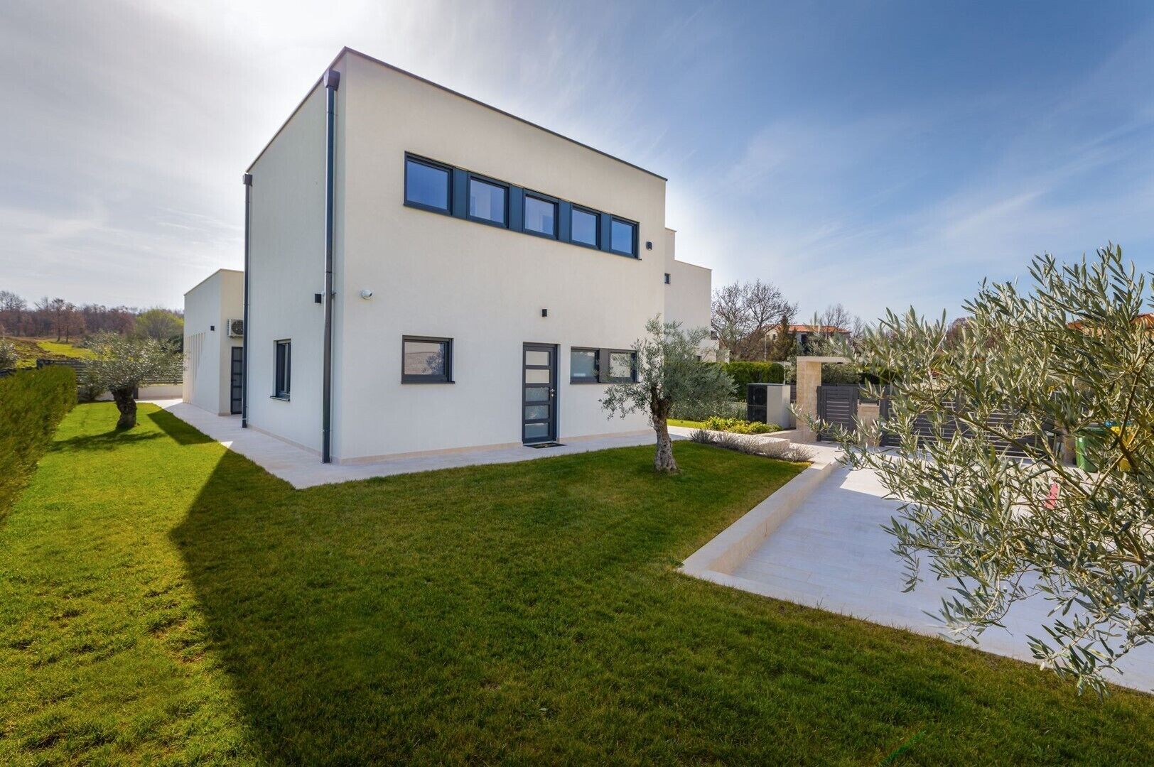 Une maison moderne à deux étages, dotée d’un toit plat, de grandes fenêtres et d’une pelouse bien entretenue.