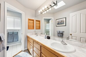 Une salle de bain moderne avec deux vasques, des meubles en bois, un grand miroir et un luminaire placé au-dessus du miroir.