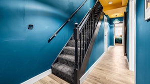 A staircase with a black handrail and carpeted steps, leading to a room with a bed and a green blanket.