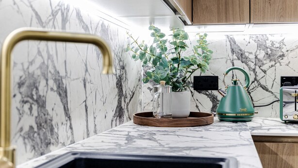 A kitchen with marble backsplash, a green kettle, a white mug, and a wooden tray.
