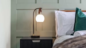 A neatly made bed with white and teal pillows, a black bedside table with a lamp, and a wooden headboard.