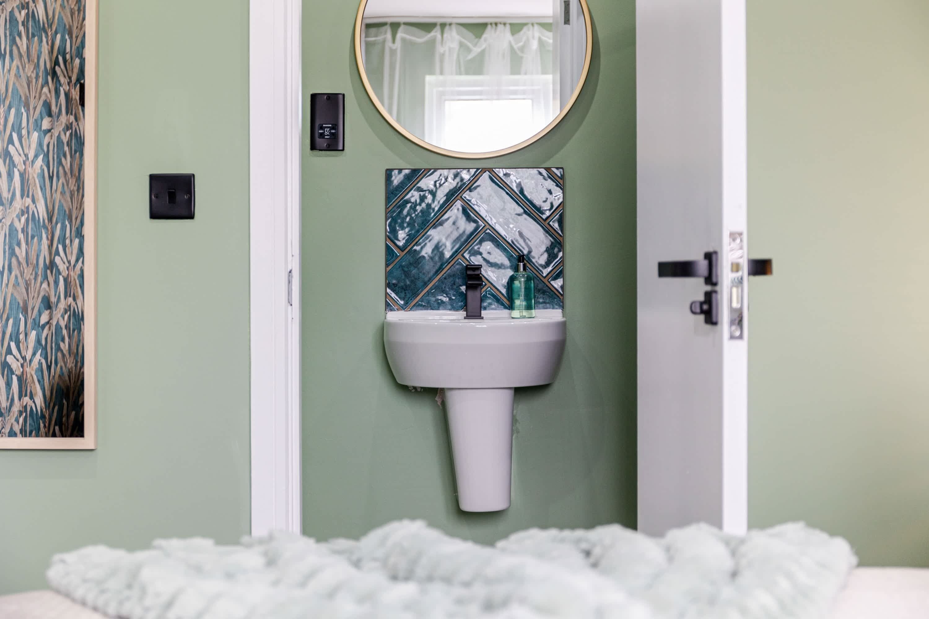 Ein Badezimmer mit einem weißen Waschbecken, einem Spiegel und einer Fliesenrückwand mit Muster.