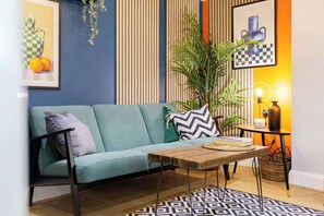 A modern living room with a teal sofa, patterned cushions, a wooden coffee table, and a patterned rug.