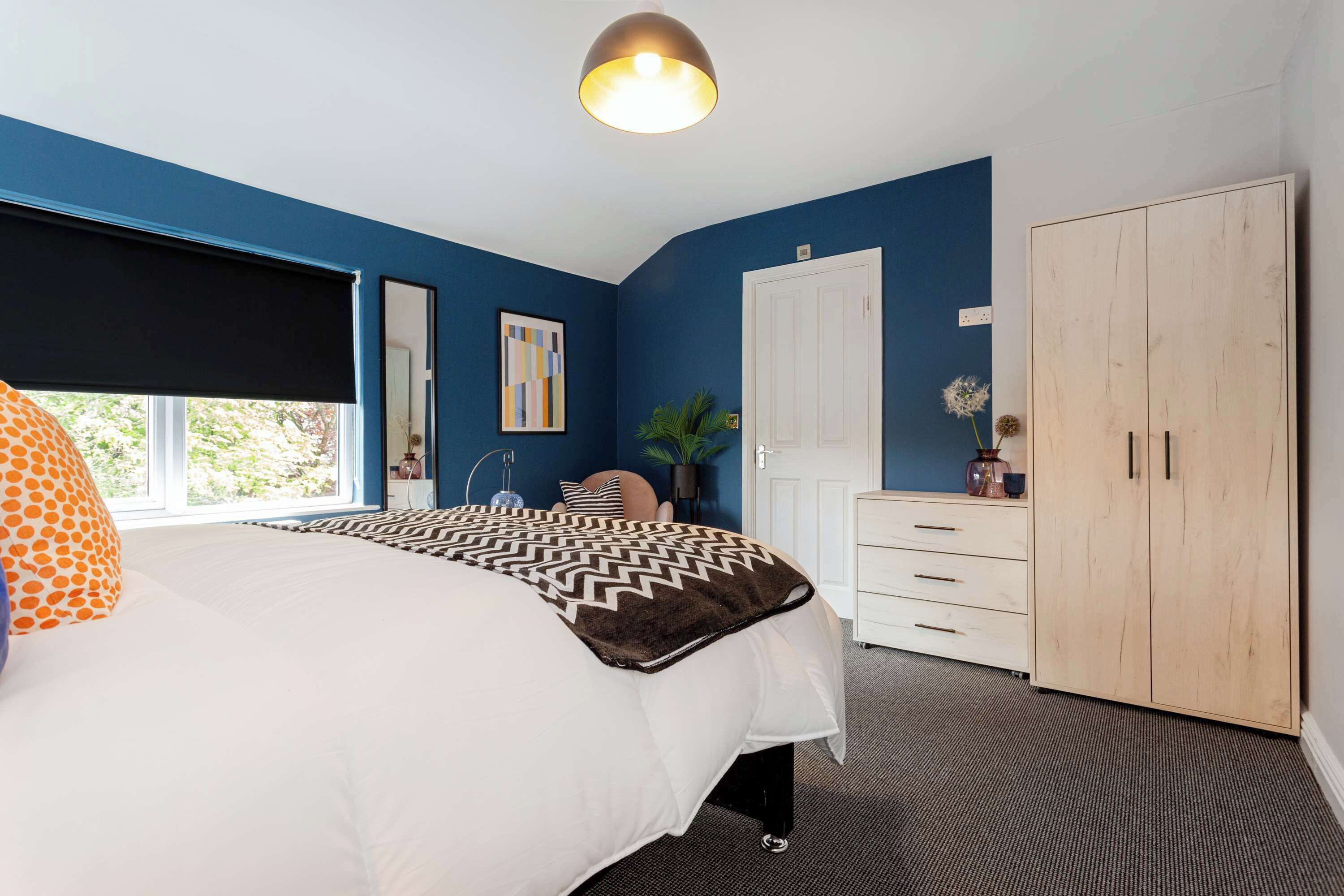 A bedroom with a bed, a wardrobe, a desk, and a window.