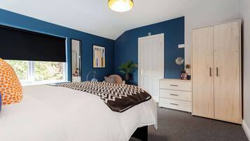 A bedroom with a bed, a wardrobe, a desk, and a window.