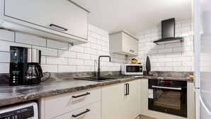 Une cuisine moderne avec des meubles blancs, un four à micro-ondes encastré, une machine à café et un lave-vaisselle.